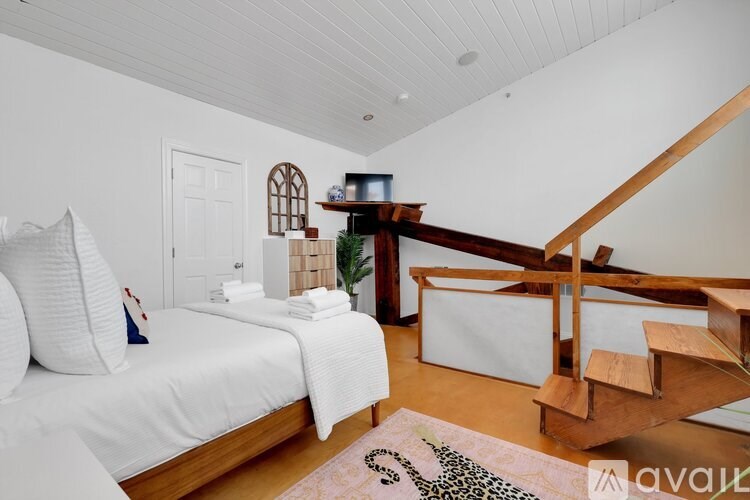 A bedroom with a white bed and a wooden staircase.