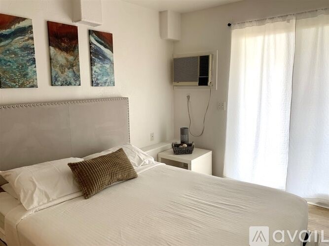 A white bed with a brown pillow and a white nightstand with a basket on it.