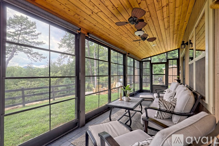 A sunroom with a ceiling fan and a view of a green lawn and trees.
