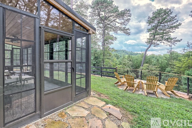 A glass-walled room with a view of a forest and a set of wooden chairs in front.