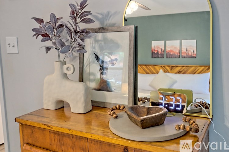 A wooden table with a mirror, a vase with leaves, and a wooden bowl with nuts on it.