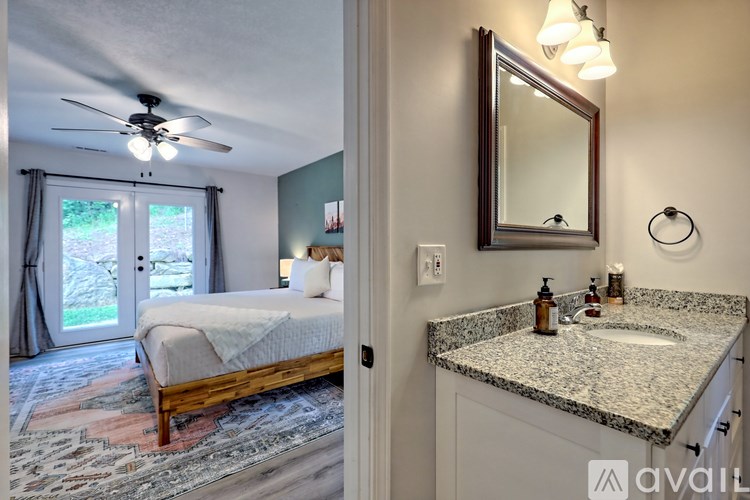 A bedroom with a bed and a bathroom with a sink and mirror.