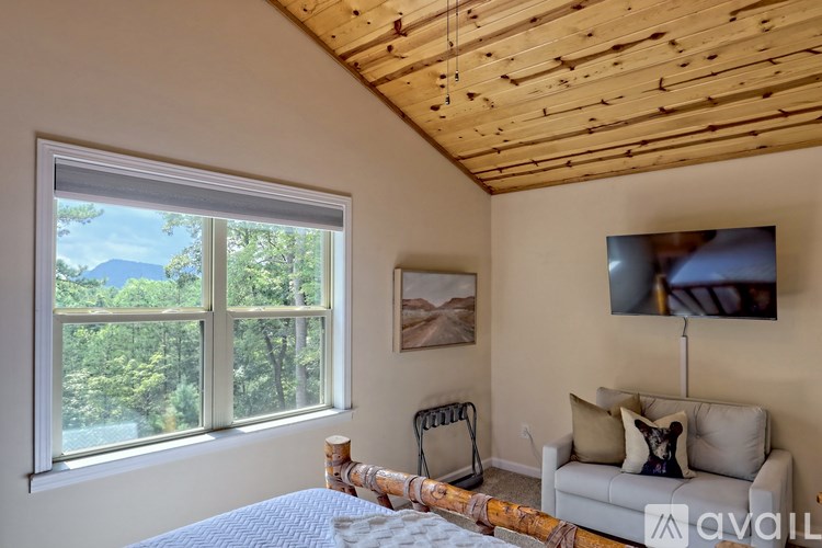 A bedroom with a bed, a couch, and a window overlooking a forest.