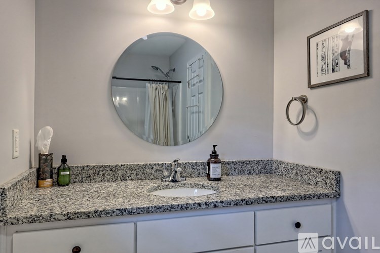 A bathroom with a granite countertop and a round mirror.