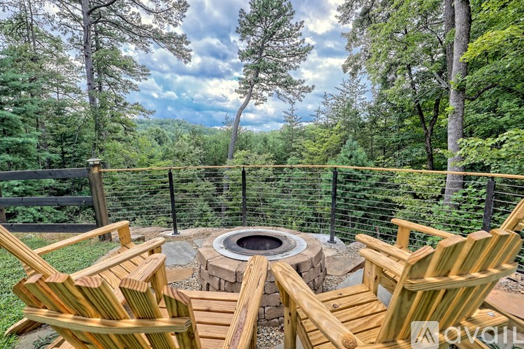 Two chairs are facing a fire pit on a deck with a forest view.