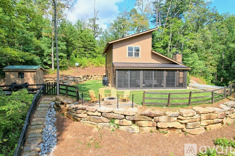 A house with a stone wall and a green roof is surrounded by trees.