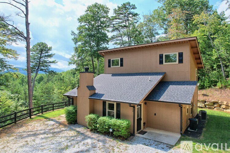 A house with a brown roof and a black grill is surrounded by greenery.