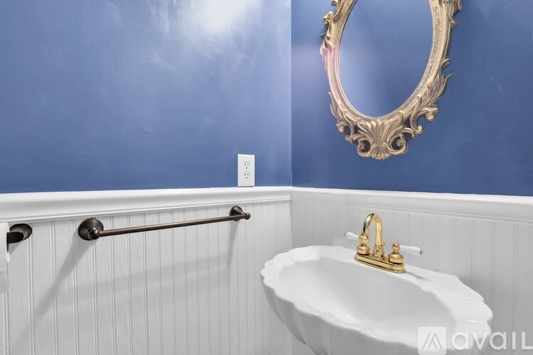 A white sink with gold faucet in a blue wall bathroom.