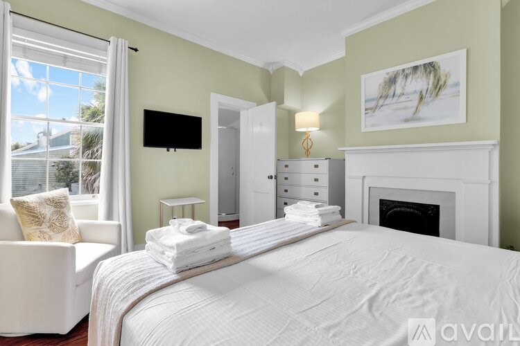 A bedroom with a large bed, a white chair, and a television on the wall.