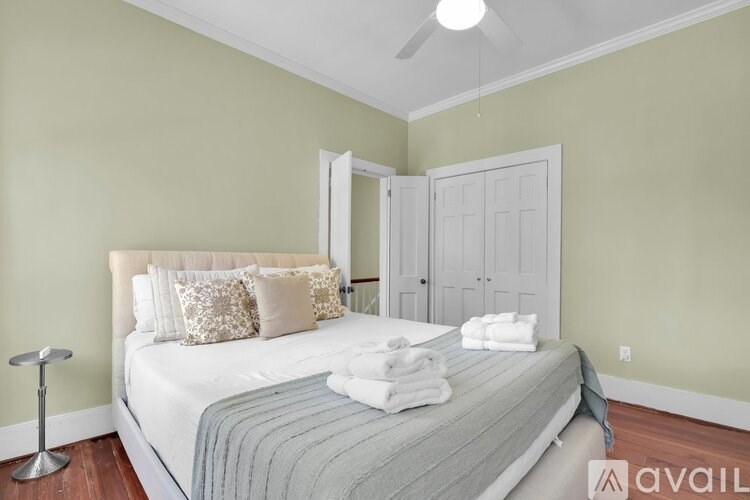 A bedroom with a bed, pillows, towels, and a fan.