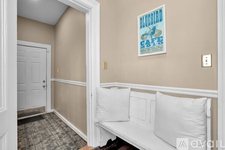 A white bench with two pillows sits in a room with a blue bird cafe poster on the wall.