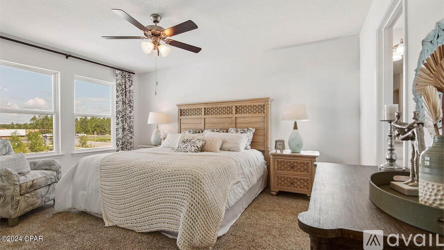 A bedroom with a large bed, a ceiling fan, and a view of the outdoors through the window.