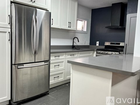 A modern kitchen with a stainless steel refrigerator and white cabinets.