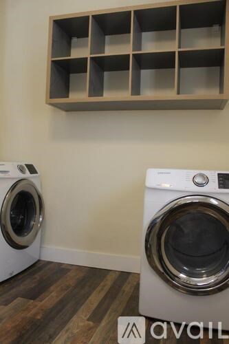 Two washing machines in a laundry room with a shelf above them.