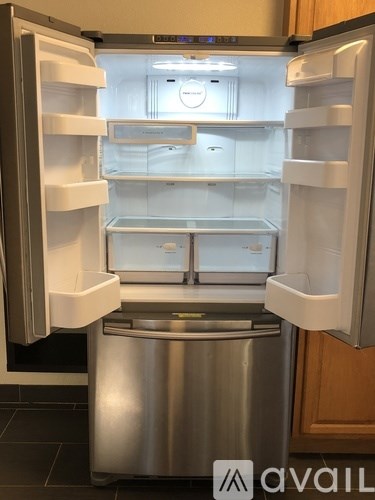A stainless steel refrigerator with its door open and a trash bin in front of it.
