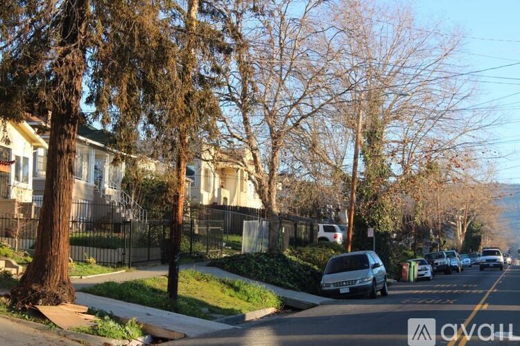A residential street with houses on both sides and cars parked along the curb.