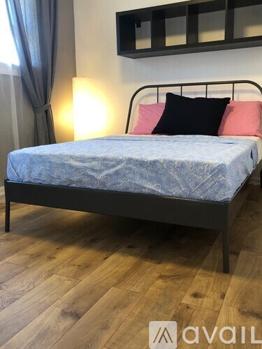 A bed with a blue bedspread and pink pillows is in a room with wooden flooring.