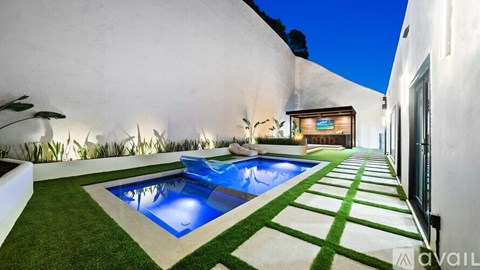 A modern outdoor pool area with a green lawn and a white wall.