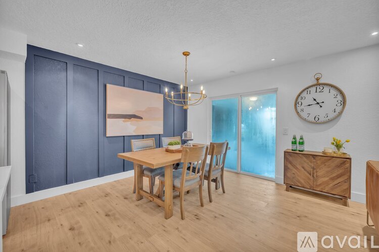 A dining room with a wooden table and chairs, a chandelier, and a clock on the wall.