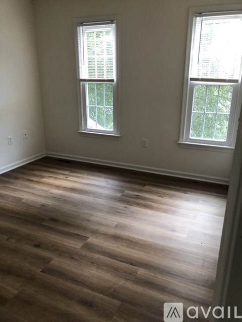 A room with wooden flooring and two windows.