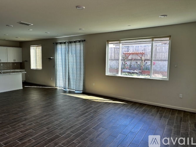 A spacious room with wooden flooring and a large window overlooking a backyard.