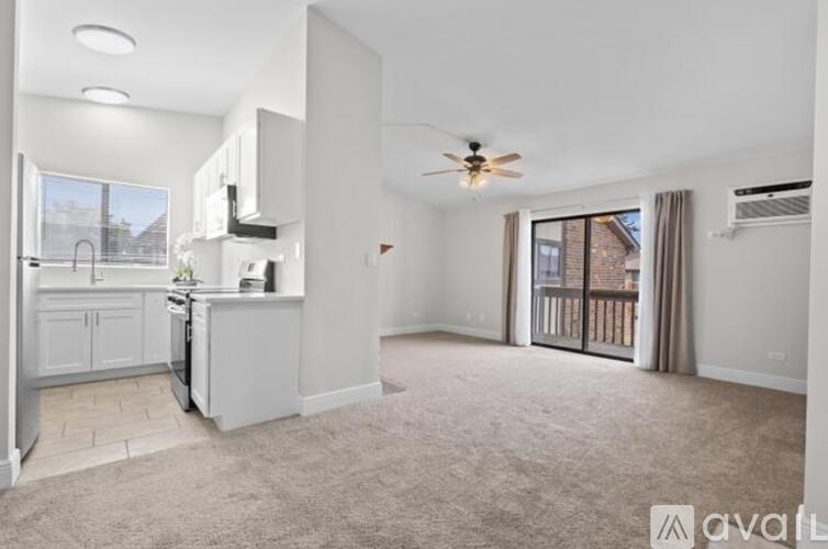 A spacious living room with a kitchen area to the left and a sliding glass door leading to a balcony.