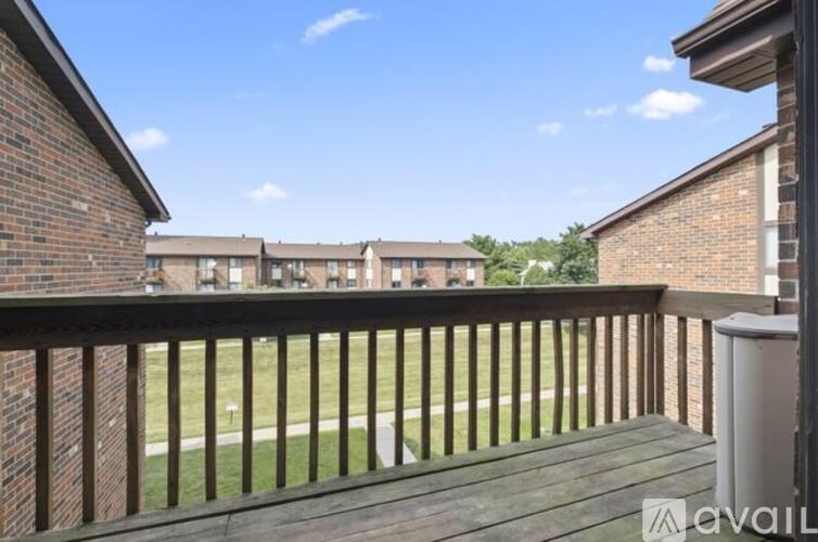 A balcony with a railing overlooks a grassy area and apartment buildings.
