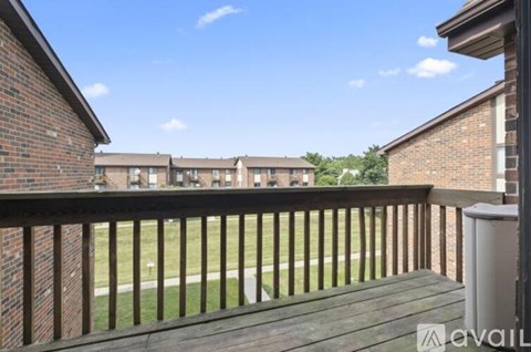 A balcony with a railing overlooks a grassy area and apartment buildings.