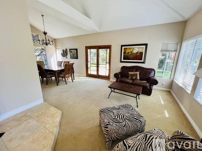 A living room with a zebra print ottoman and a brown leather couch.