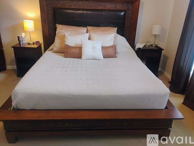 A bed with a white comforter and four pillows sits on a wooden platform in a room with two lamps on either side.