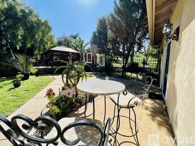 A patio with a table and chairs is surrounded by greenery.