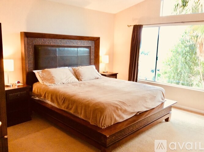 A bedroom with a large bed and a window overlooking greenery.