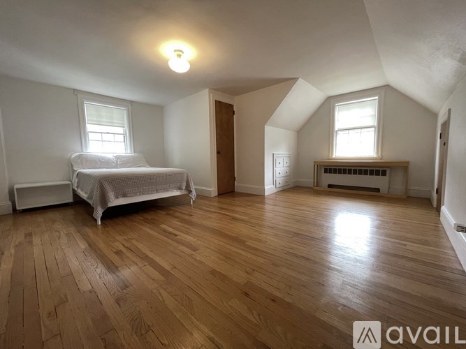 A room with wooden floors and white walls has a bed and a window.
