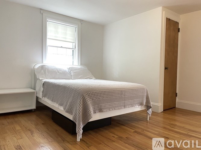 A bedroom with a bed, a window, and a wooden floor.