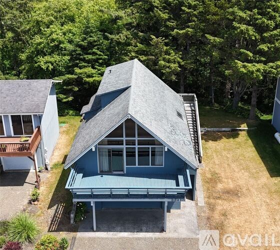 A house with a blue roof and a deck is surrounded by trees.