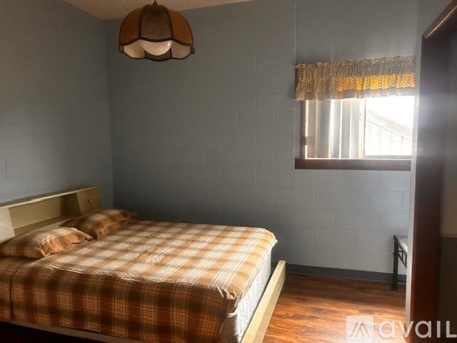 A bedroom with a bed, a window with a curtain, and a ceiling light.