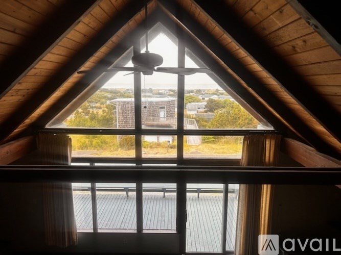 A view from inside a wooden structure looking out through a window at a building and trees.