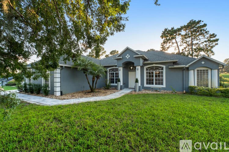 A house with a grey exterior and a white roof is surrounded by greenery.