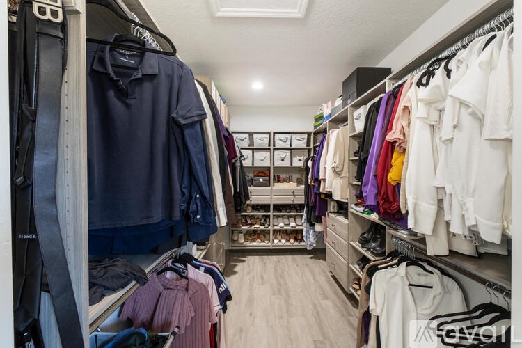 A walk in closet with clothes hanging and drawers underneath.
