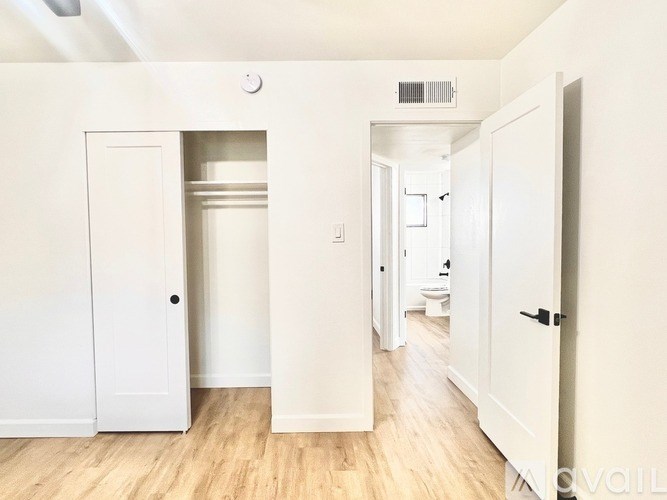 A white hallway with a door on the left and a toilet in the distance.