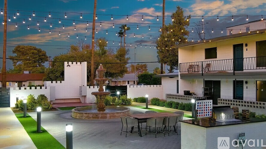 A courtyard with a fountain, chairs, and a table is illuminated by string lights.
