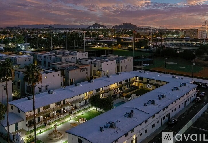 A large white building with a fountain in the middle of a courtyard is lit up at dusk.