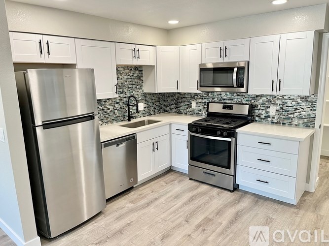 A kitchen with a stainless steel refrigerator, microwave, oven, and white cabinets.