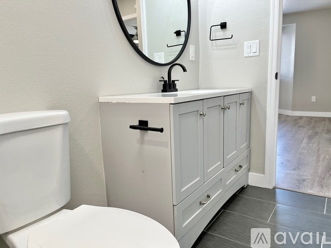 A bathroom with a white toilet, a round mirror, and a cabinet with a black handle.