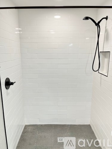 A white tiled bathroom with a black shower head and handle.