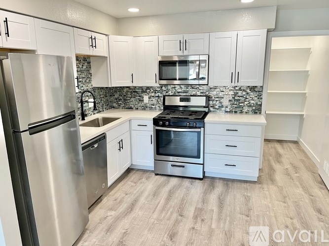 A kitchen with a stainless steel refrigerator, microwave, oven, and white cabinets.