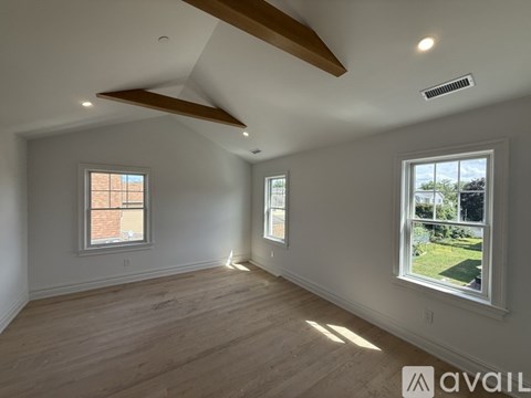 A spacious room with wooden floors and two windows.