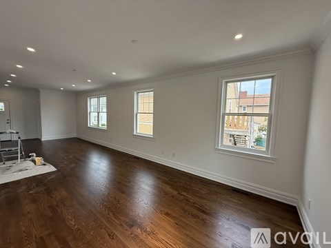 A room with wooden floors and white walls, with two windows and a ceiling with wooden beams.