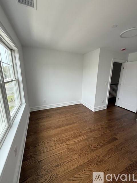 A room with wooden flooring and two windows overlooking a street.