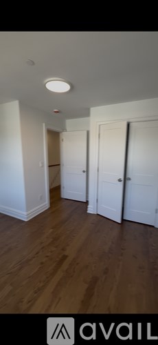 A room with wooden flooring and white walls, with a door and a window.